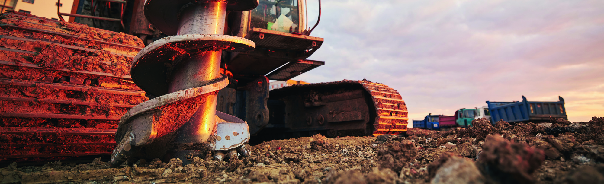 Building activity on contruction site. Close-up view of drilling machine against trucks. 